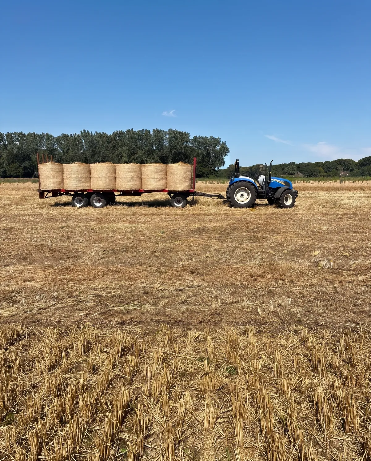 Een trekker met een wagen vol ronde balen hooi op het land van Van Vlerken