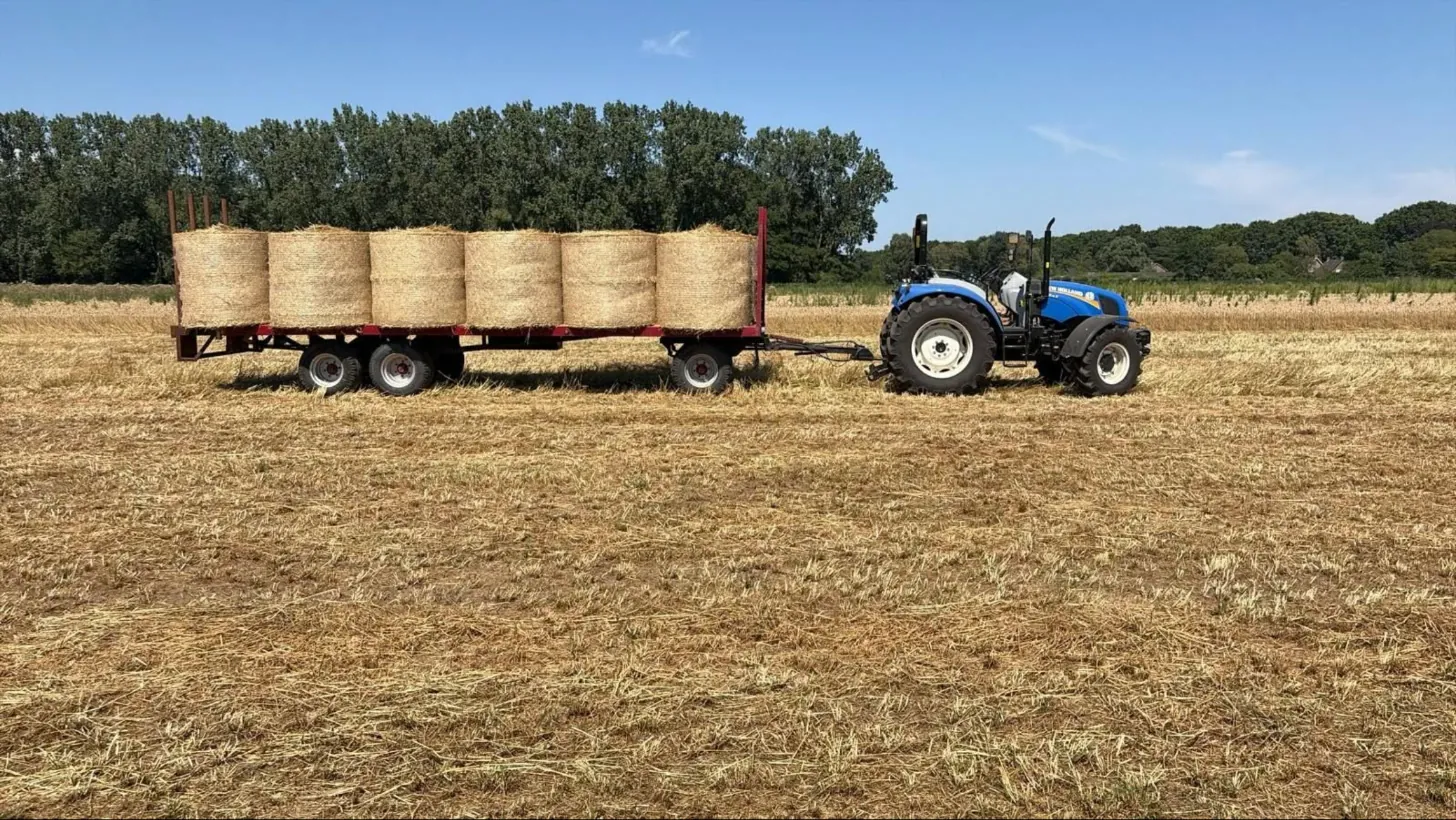 Een trekker met een wagen vol ronde balen hooi op het land van Van Vlerken